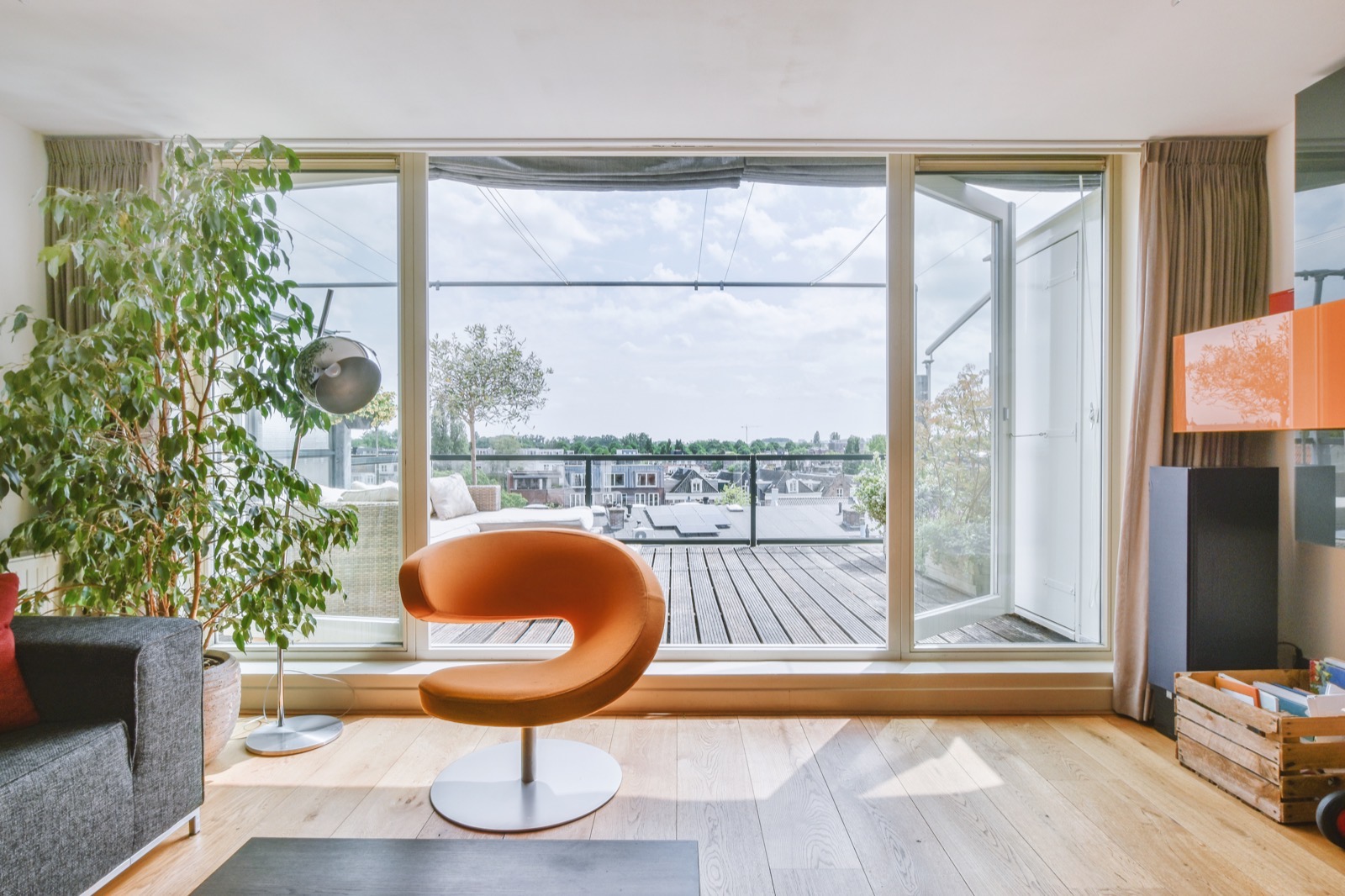 Sala luminosa de um apartamento com uma grande porta envidraçada para um terraço e os telhados da cidade